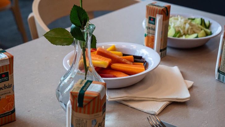 Ett dukat bord med en blomvas, en skål med morötter och apelsinsaft.