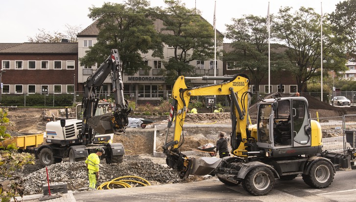 två grävmaskiner har grävt upp asfalt vid vägarbete, personer med gula varselkläder