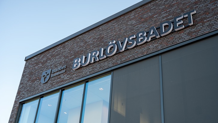Bilden föreställer fasaden på Burlövsbadet. Mörkgrå tegel och stora fönster. Burlövs kommuns logotyp och texten Burlövsbadet är skyltat på fasaden.