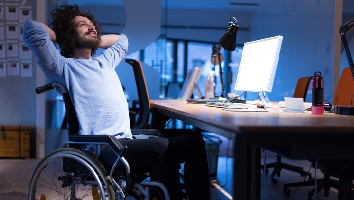 En man som sitter i rullstol framför ett skrivbord med en datorskärm.