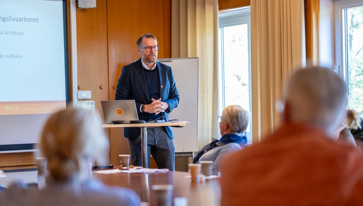En man som står vid ett talarstativ framför en grupp människor.