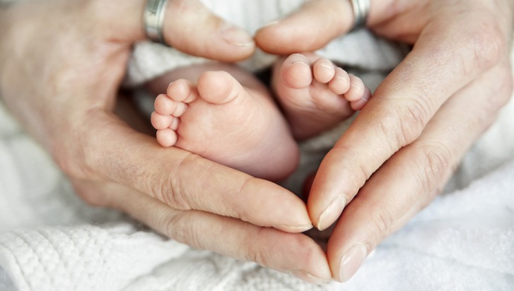 Ett par händer utformade som hjärta omringar små, nyfödda fötter