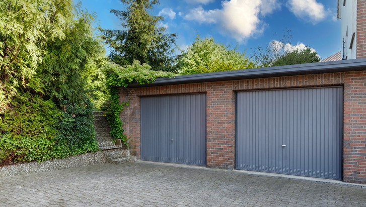 Modern parking garage in residential brick house for cars with grey roller shutters on gates. Closed doors in garages.