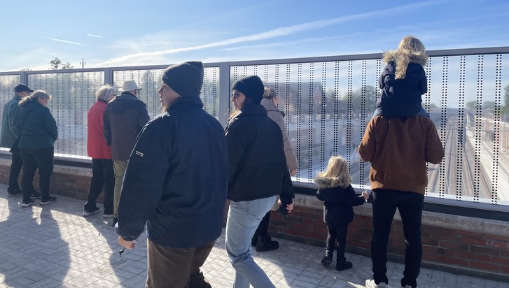Människor promenerar förbi samt tittar ner på de nya järnvägsspåren i Åkarp.