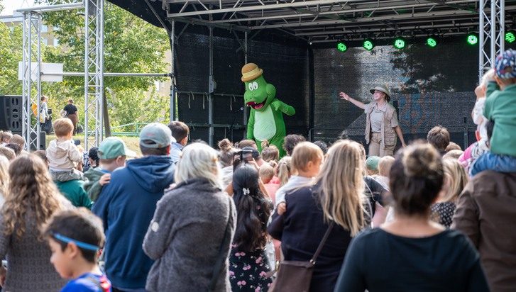 En stor grupp människor som står framför en scen. På scenen står en person i alligator-kostym.
