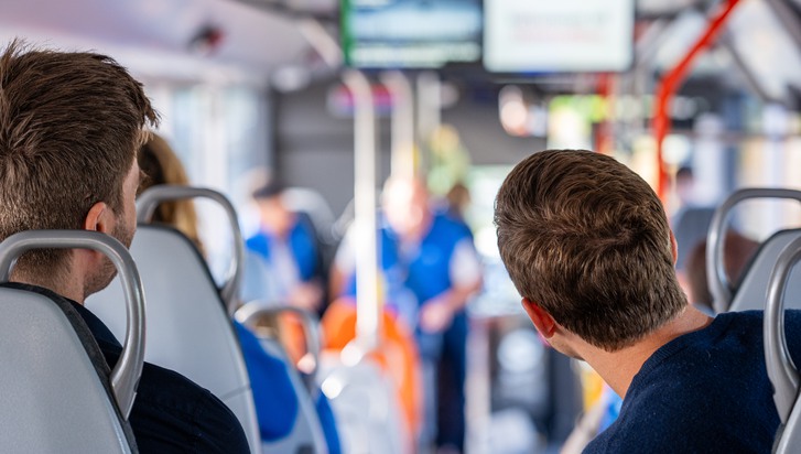 Två personer sitter på en buss och tittar fram, ut mot vägen. I bakgrunden syns fler personer sittandes på bussen.