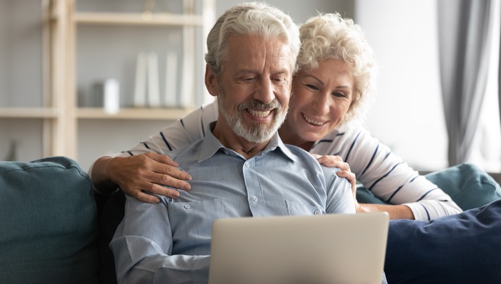 Äldre par sitter i soffan och tittar leende på en datorskärm