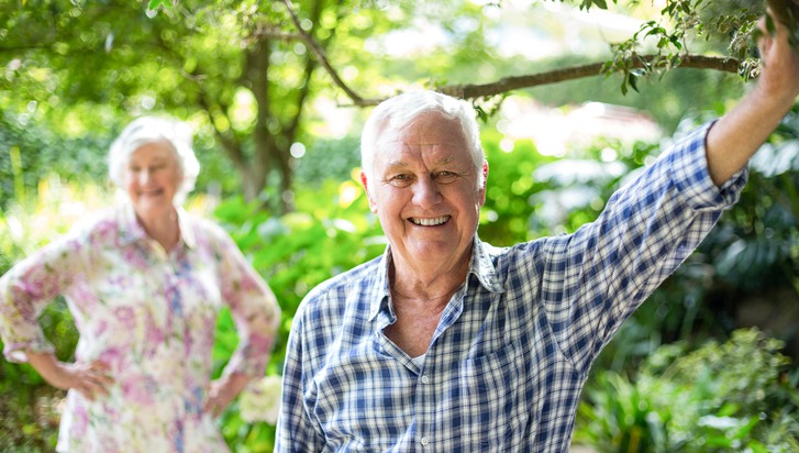 Portrait of senior man with wife standing in background at back yard