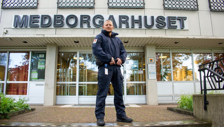 trygghetsvärd i mörkblå uniform poserar framför entrén till Medborgarhuset