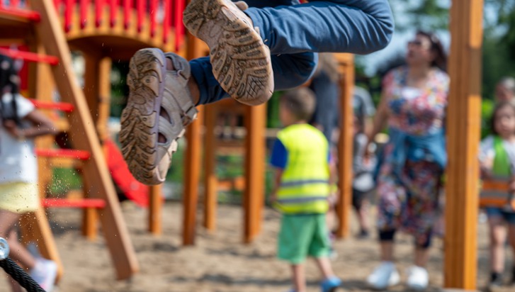 Barn som leker på en lekplats. I förgrunden ser man benen och skorna på ett barn som hoppar högt